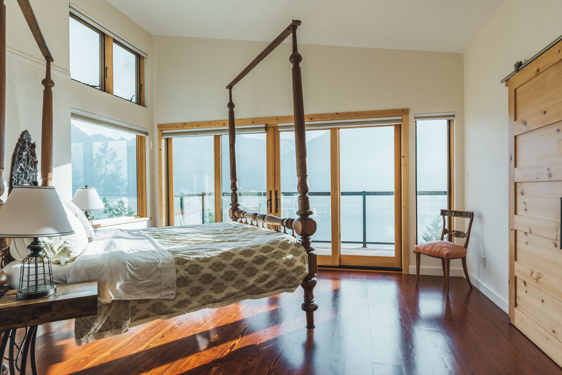Large bed and double doors looking towards the lake in a custom home built by Eisenhauer Woodworks in Kaslo BC