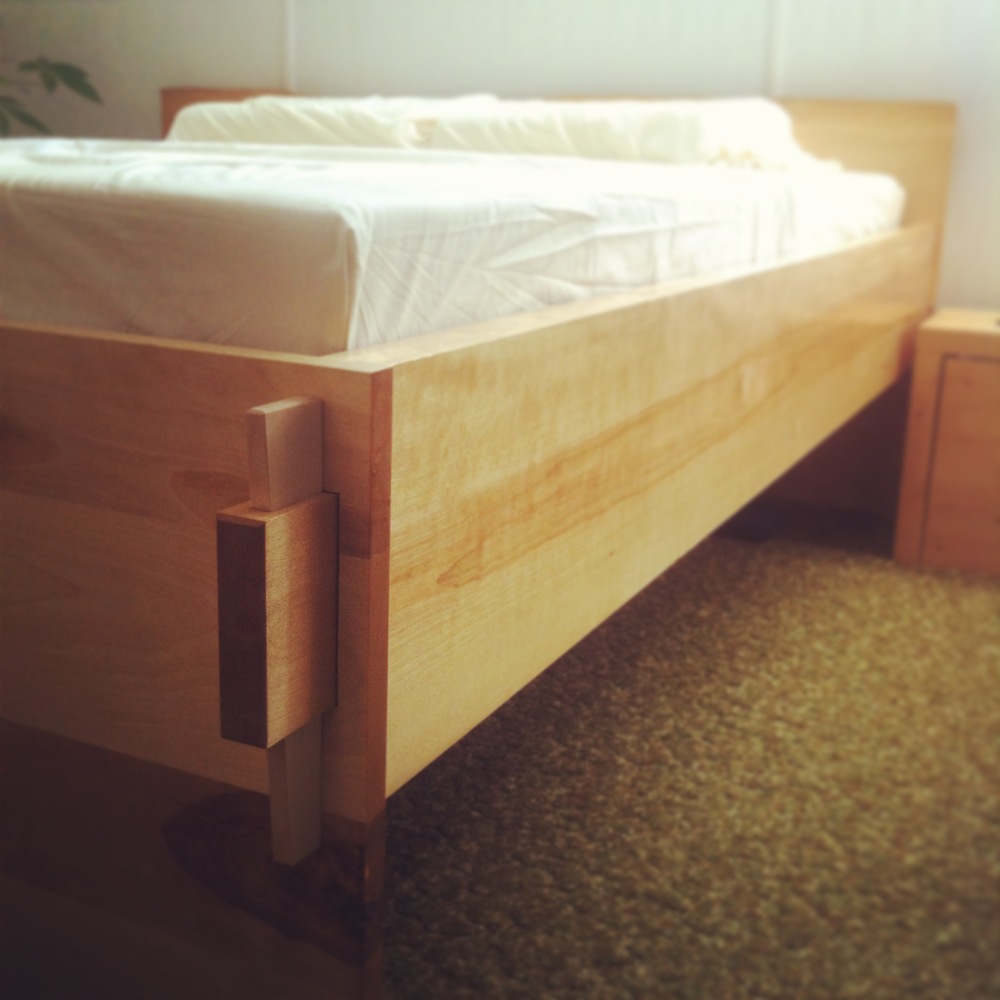 The notched corner of a custom light wood bed frame made by Eisenhauer Woodworks